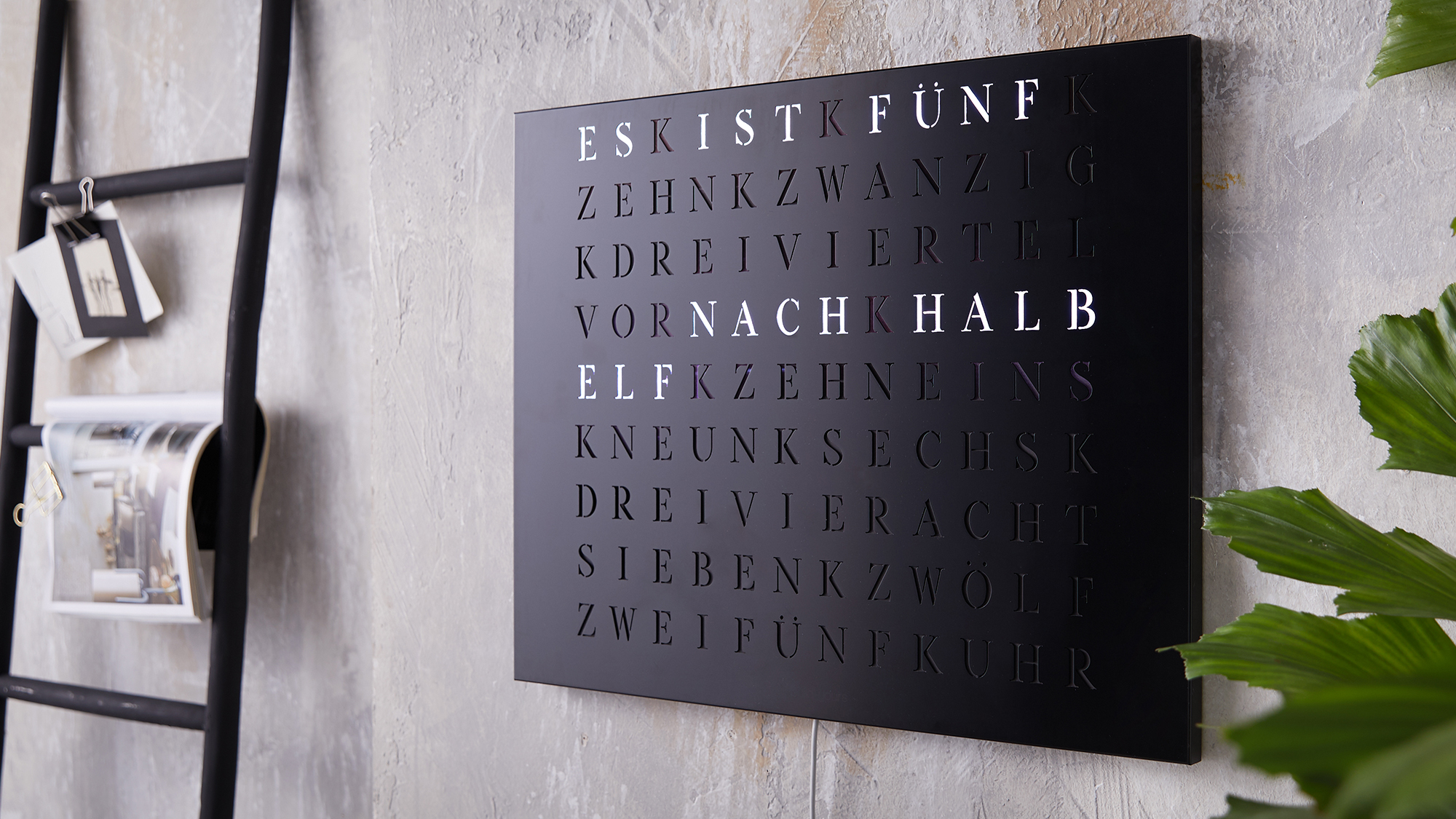 Wortuhr aus schwarzem Edelstahl hängt an einer Wand in einem modernen Apartment